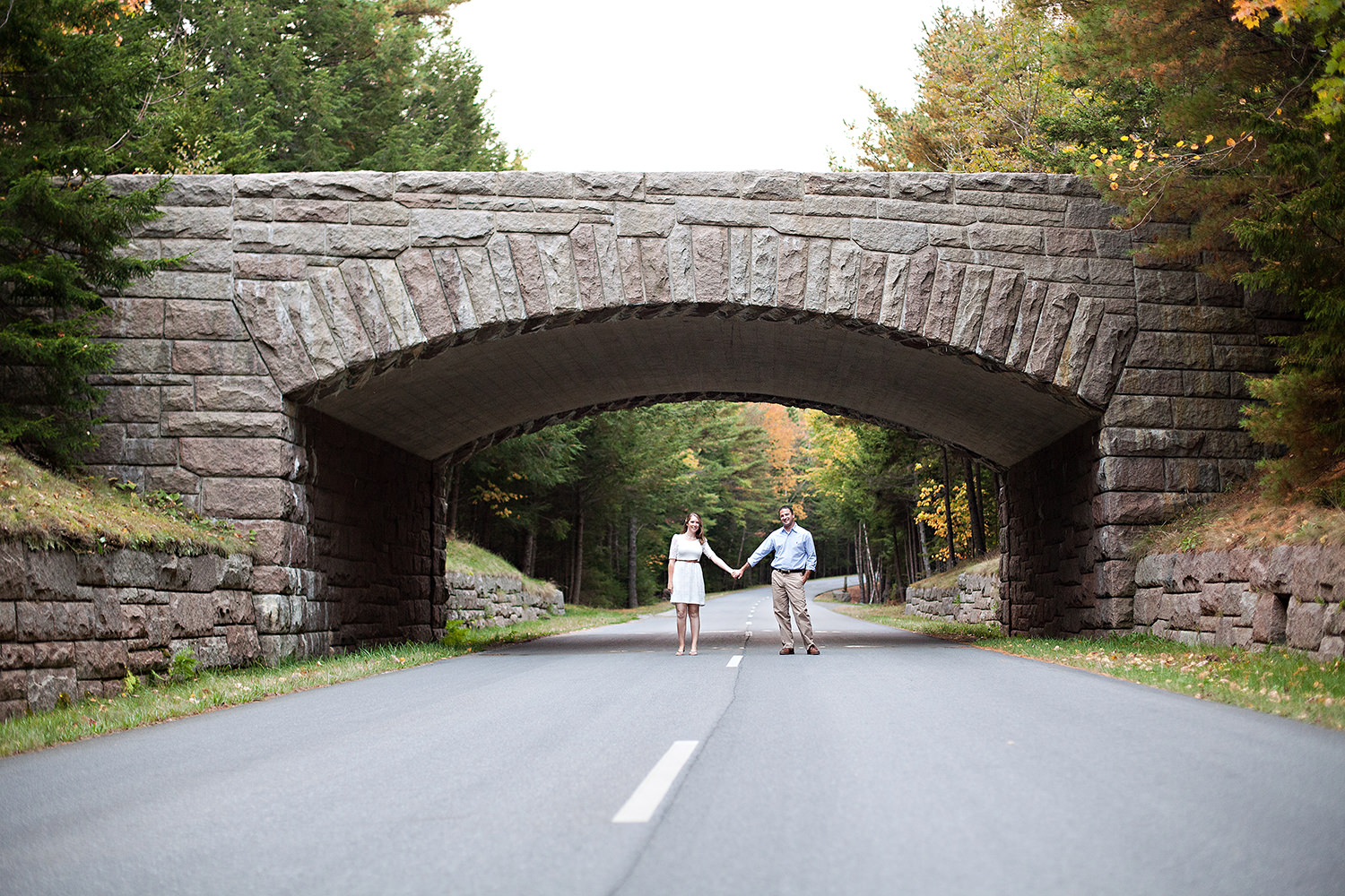 couple stand under a bride in Acadia National Park during engagement photos in Bar Harbor