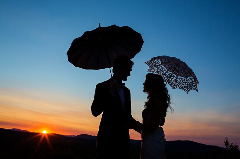 bride and groom's silhouetted against the sunset holding umbrellas at Maine wedding