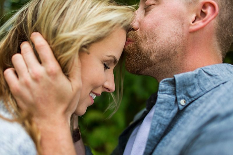 An engagement photo of a man kissing a woman's forehead.