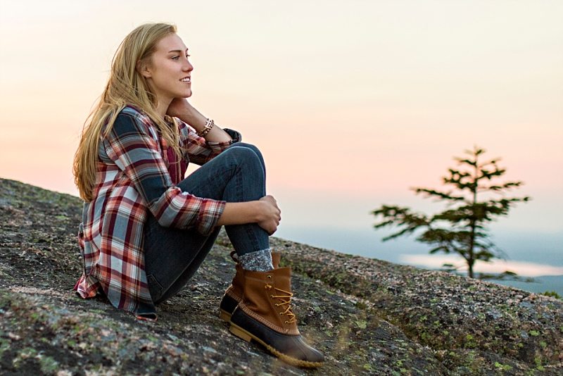 A senior portrait of a girl sitting on Cadillac Mountain at sunset.