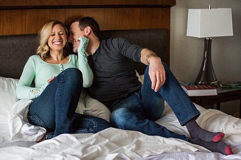 A lifestyle portrait of a couple sitting in bed and laughing together.