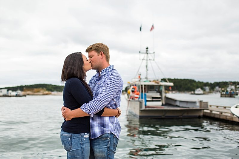 A couple kisses with boats in the background in Stonington, Maine.