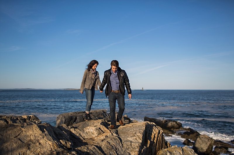 A couple walks together on the cliffs at Portland Head Light.