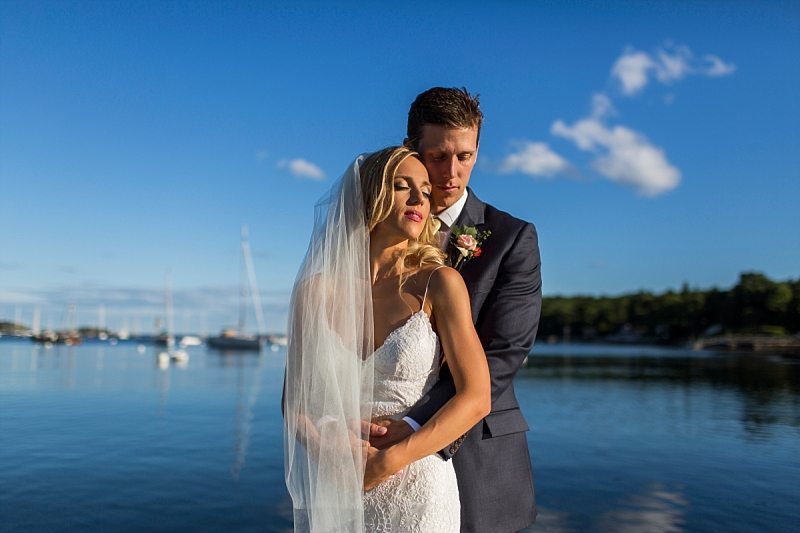 A bride and groom let the sun warm their faces at Rockport Harbor in Maine.