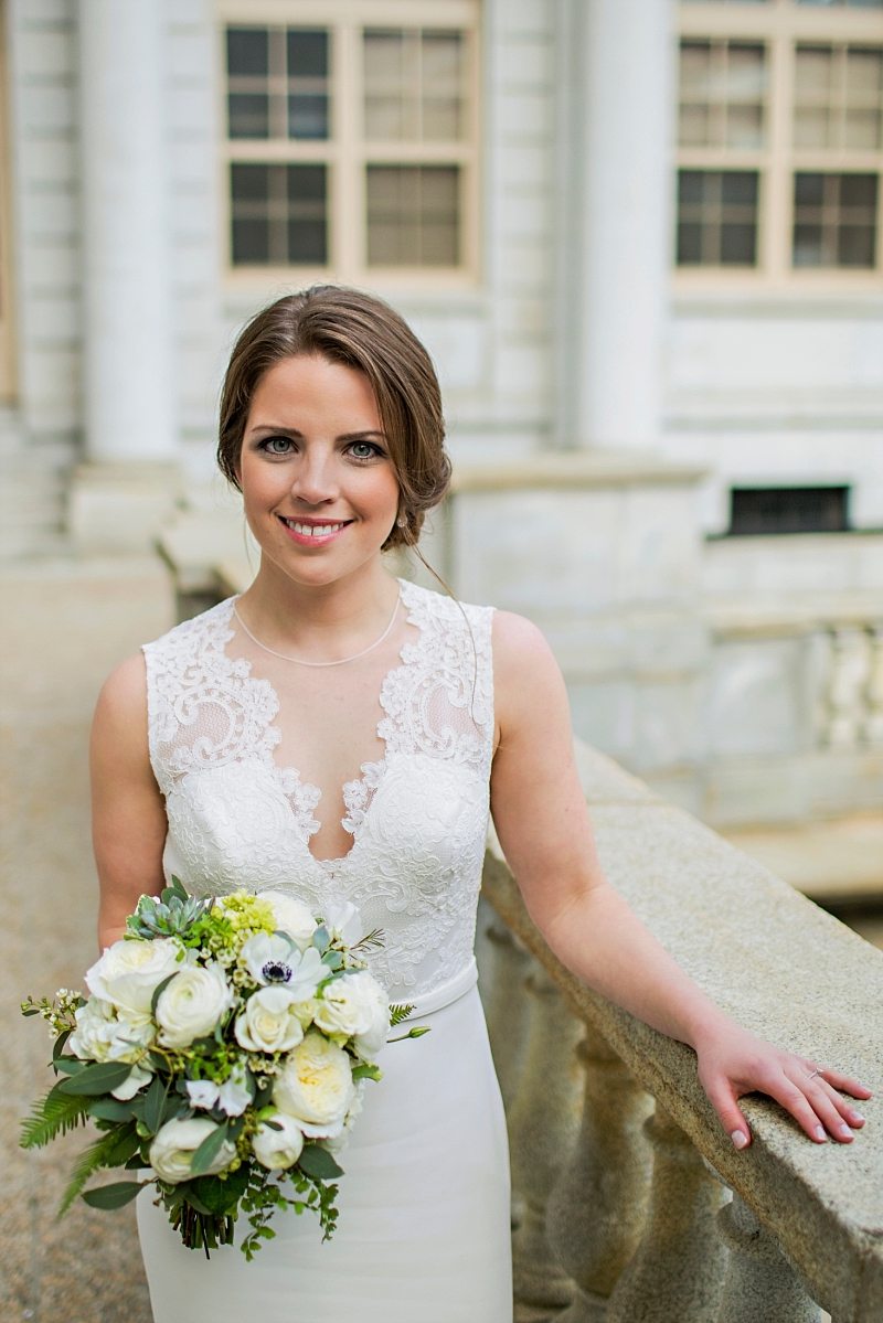 A posed portrait of a bride smiling outside Portland Maine City Hall with her bouquet.