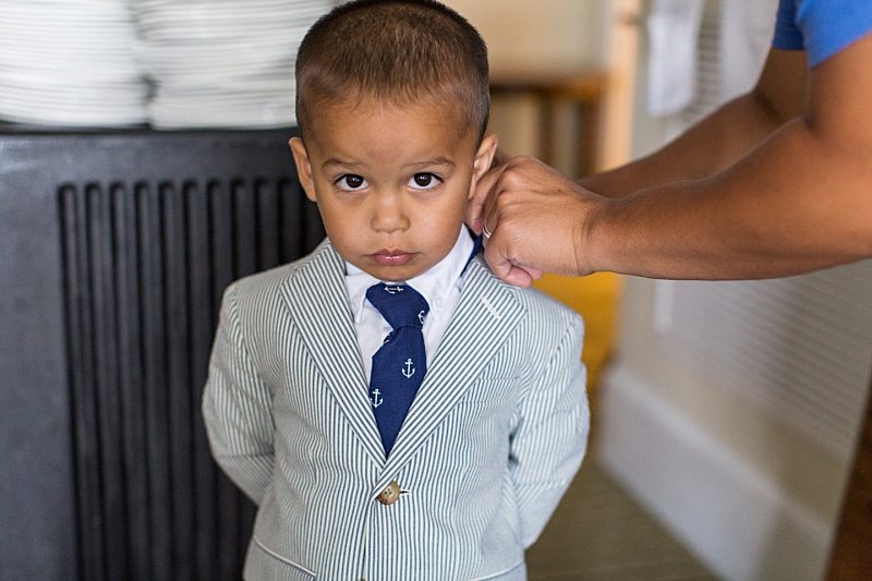 A photo of a little boy at a wedding having his collar adjusted.