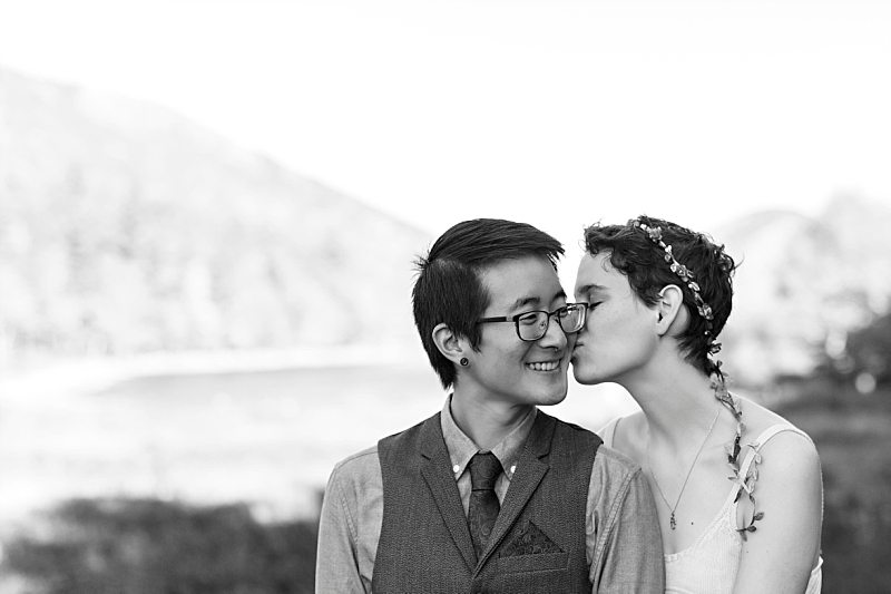 A black and white portrait of a bride kissing the groom on the cheek at Jordan Pond in Acadia National Park.