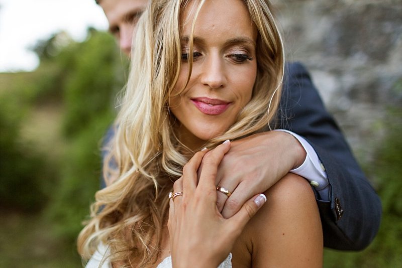 A close up of a bride's face as she holds the groom's hand on her shoulder, showing off both wedding bands.