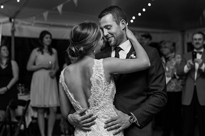 A black and white image of a couple dancing their first dance at their wedding after ten years together. They smile and look deep into each other's eyes.