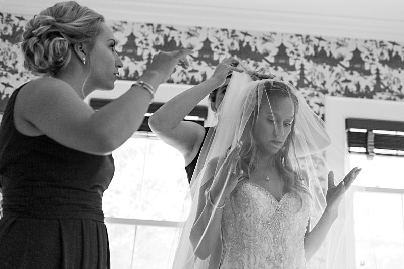A black and white photo of a bride's sister and future sister-in-law placing her veil in her hair.