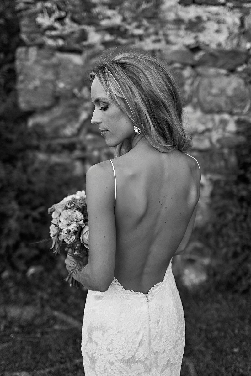 A black and white portrait of a bride looking over her shoulder with in a backless wedding gown.