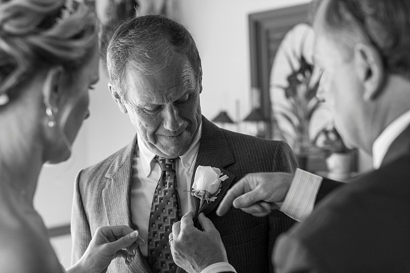 The bride and the groom's father try to pin a boutonniere on the bride's father.