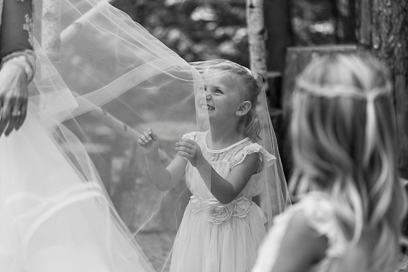 A black and white photo of a flower girl playing in the bride's veil.