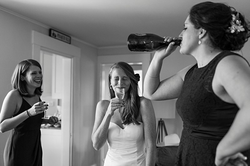 A bride and her bridesmaids laugh as they finish a bottle of champagne before the wedding ceremony.