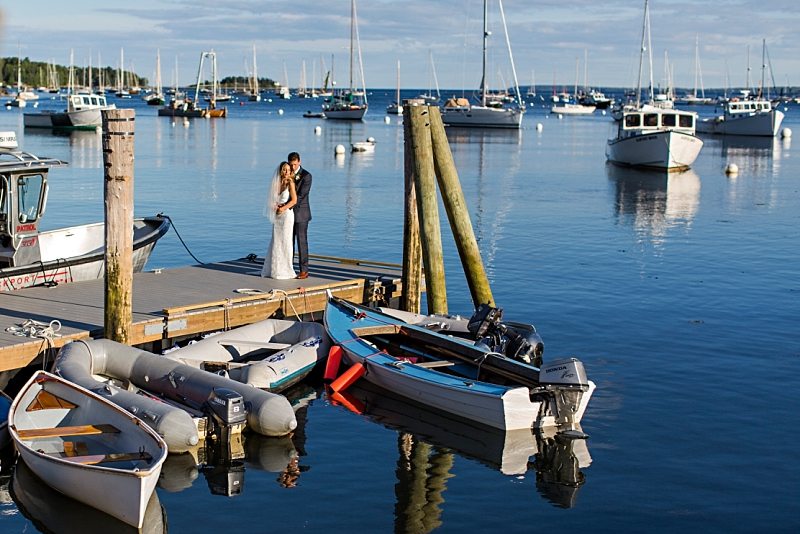 A bride and groom embrace in a scenic shot showing Rockport Harbor in Maine.
