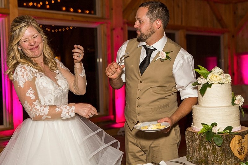 A bride wrinkles her nose and laughs as the groom tries to smear cake on her face.