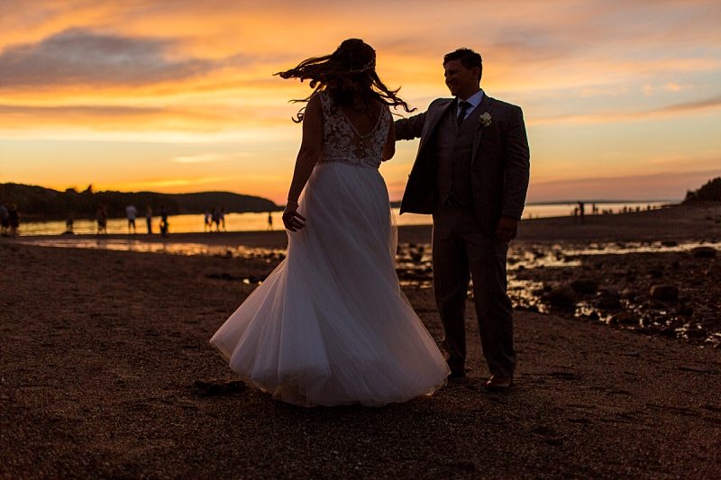A silhouette of a groom twirling a bride at sunset.