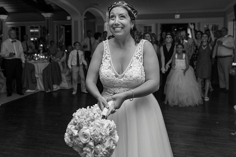 A bride smiles widely as she stats to throw her bouquet.