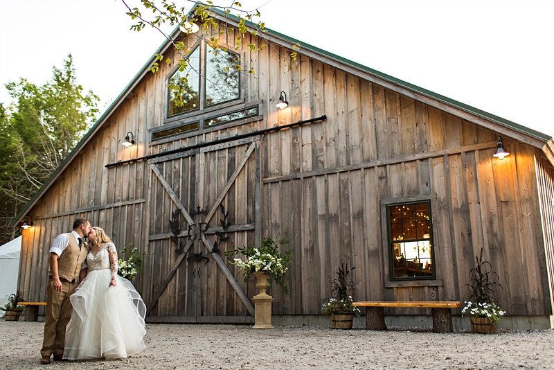 A bride and groom kiss in front of the barn at Granite Ridge Estate & Barn in Norway, Maine.