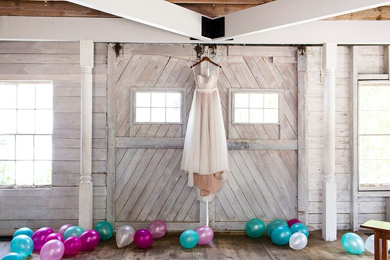 A wedding dress hangs in the white-washed barn at Hardy Farm surrounded by balloons.