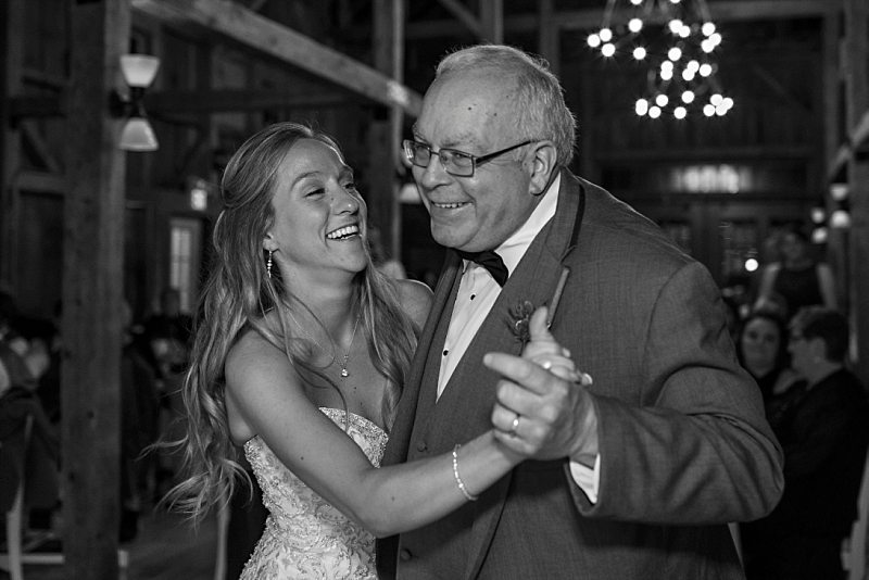 A bride and her father laugh as they dance together at the reception.