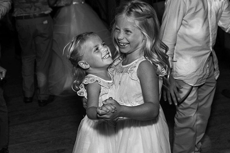 Two flower girls dance together and laugh at a wedding reception.
