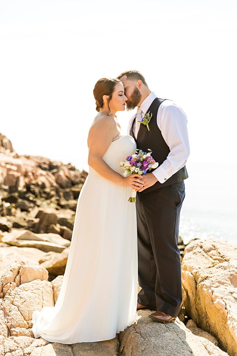 A bride and groom kiss on the cliffs of Acadia National Park.