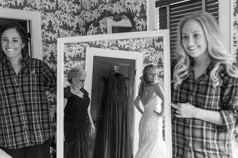 Two bridesmaids hold a mirror as the bride and her mother admire her in her wedding gown.