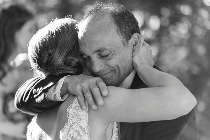 The father of the bride tears up as his daughter hugs him.