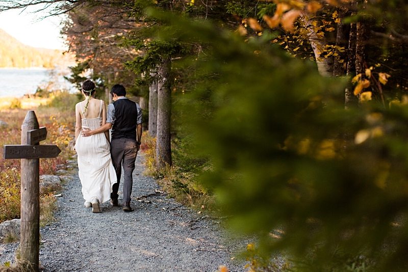 The groom puts his arm around the bride as they walk along the trail at Jordan Pond in Acadia National Park.