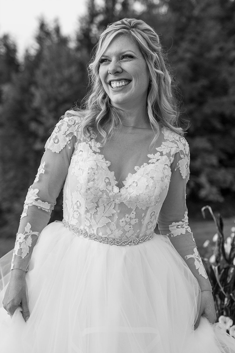 A black and white portrait of a bride as she smiles at the groom.