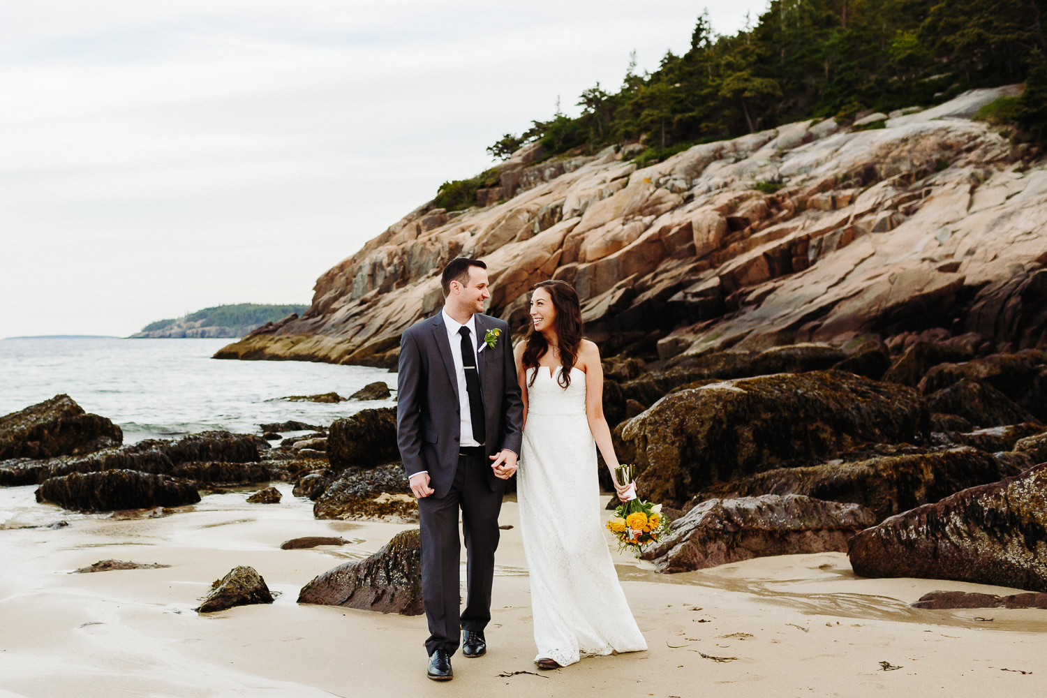 Bride and groom smiling at each other at Sand Beach after elopement at Jordan Pond in Acadia National Park