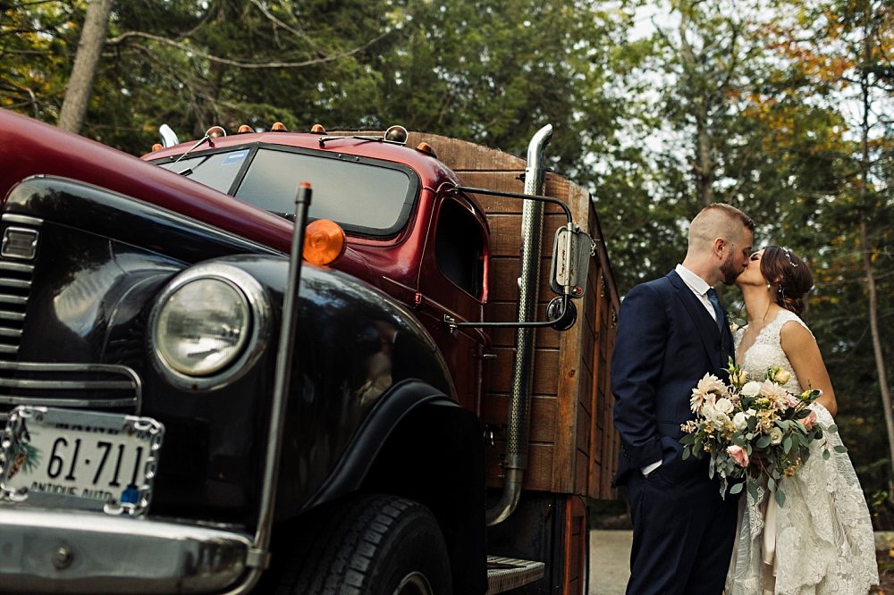 Bride and groom kissing in front of antique truck during wedding at Granite Ridge Estate & Barn