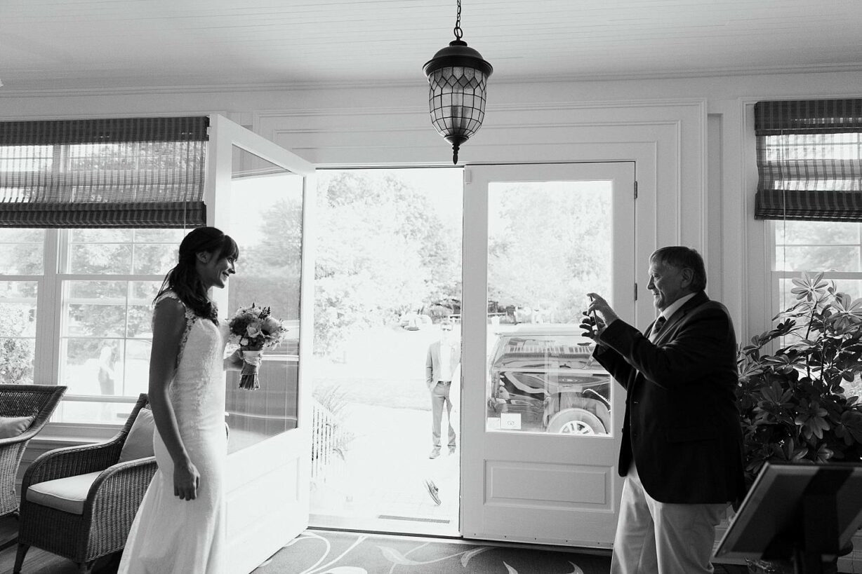 Father of the bride takes a photo of the bride before they leave for her Sand Beach Acadia elopement
