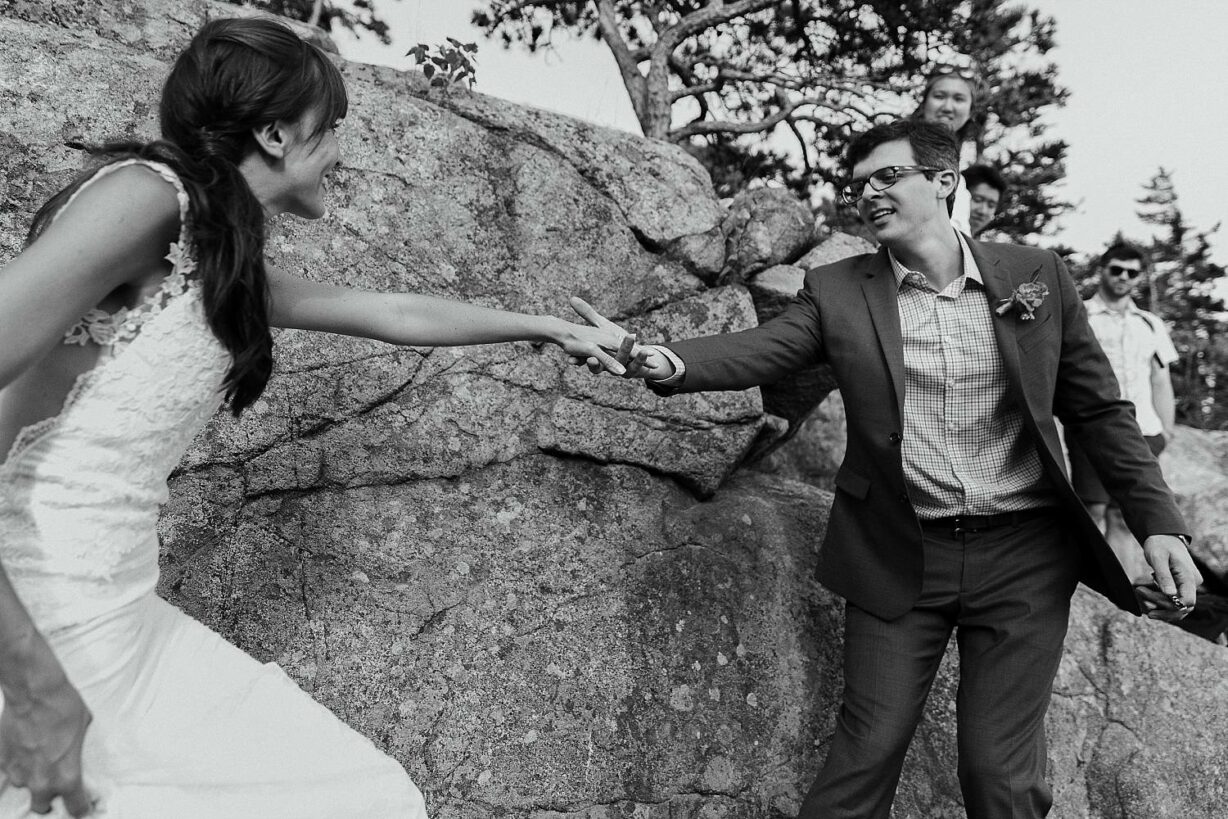 Groom reaching for bride's hand as they hike during their Acadia elopement
