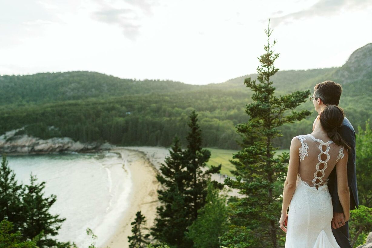 Bride and groom looking down on Sand Beach in Acadia National Park after elopement