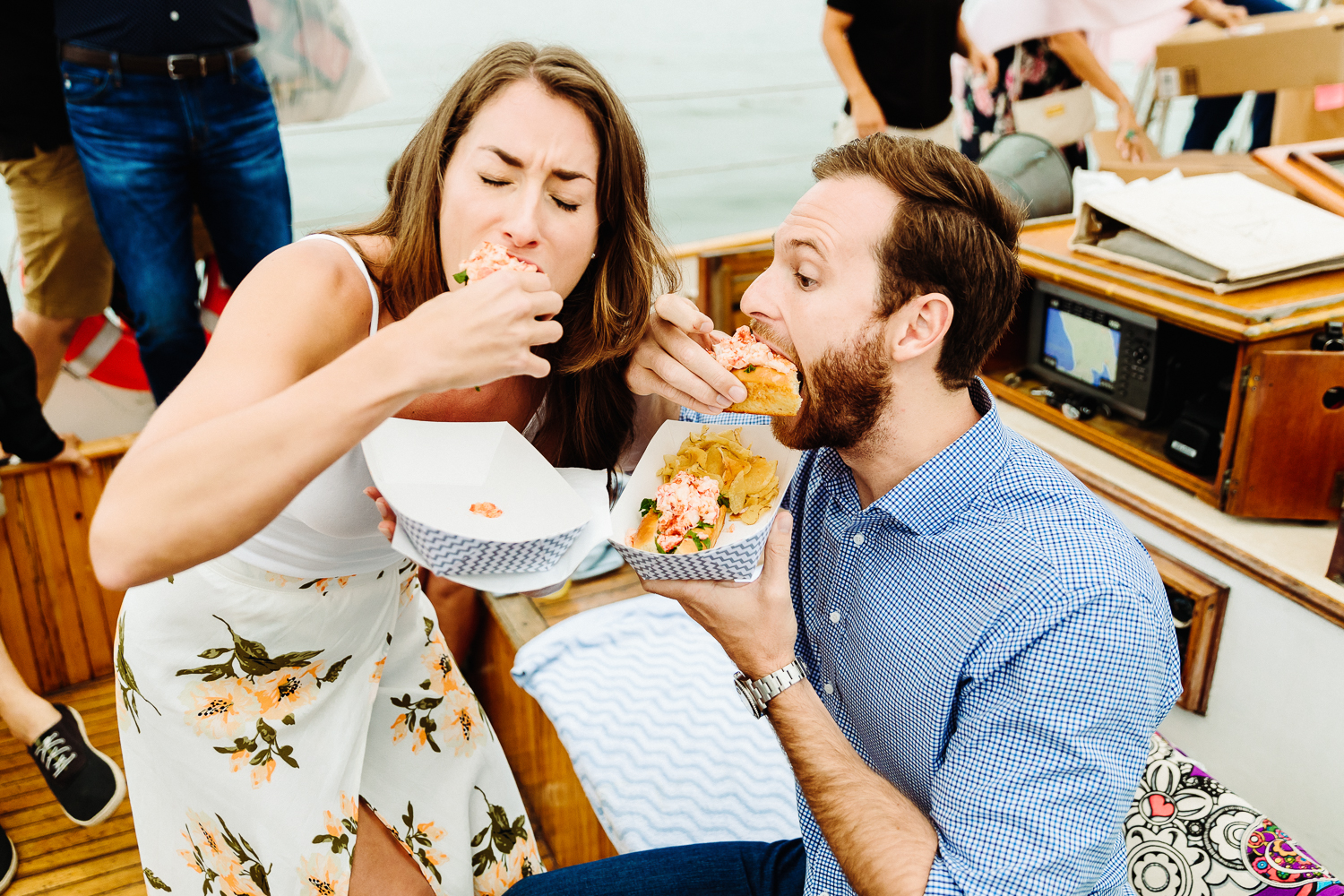 bride and groom eat a lobster roll during their Portland Maine rehearsal dinner cruise