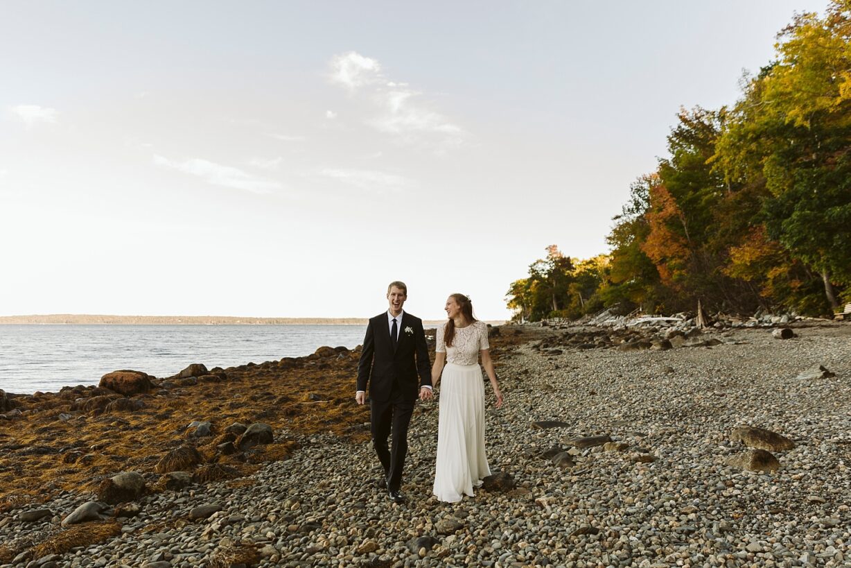 Bride and groom walking on rocky Maine beach in Northport Maine.