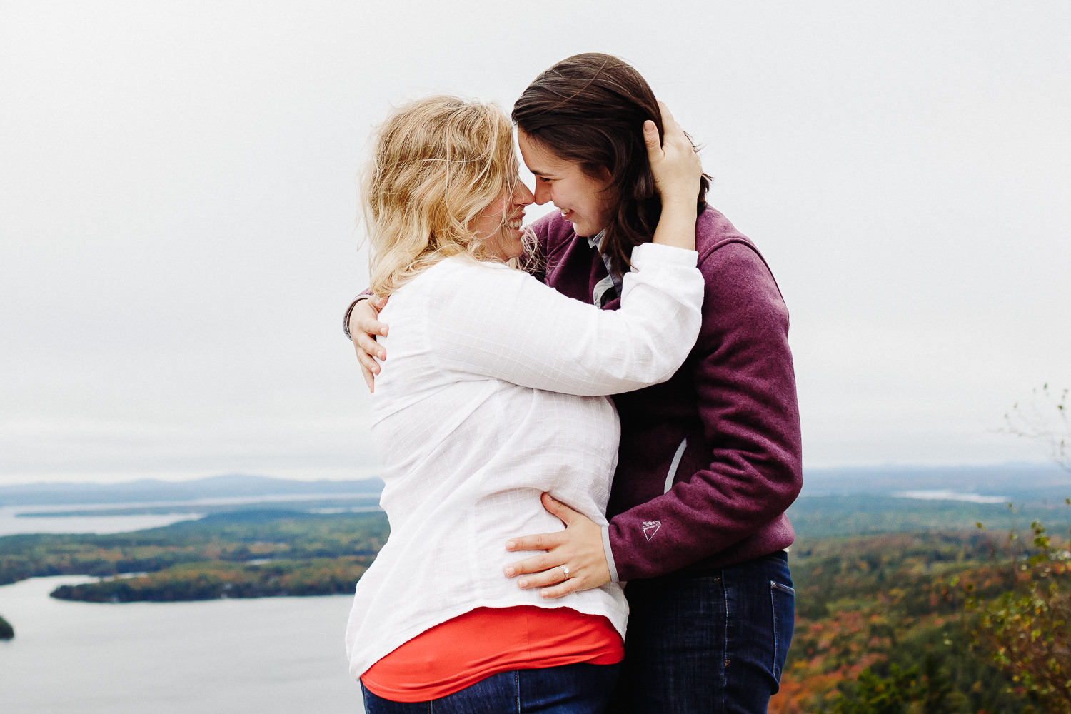 Two women going in for a kiss during engagement photos on Beech Mountain in Acadia National Park
