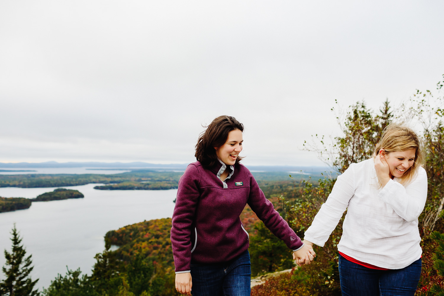 women holding hands and laughing during Beech Mountain Acadia National Park engagement photos