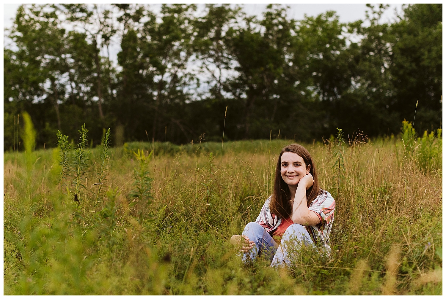 senior girl sitting in grass during senior portraits at Fields Pond Audubon