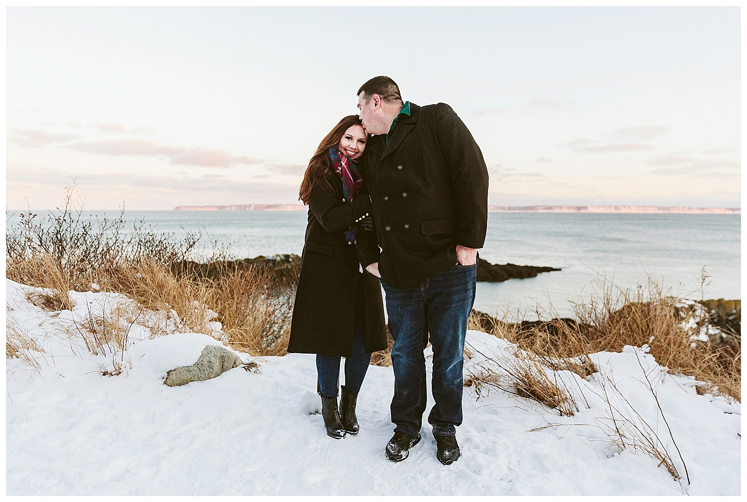 Man kissing fiancee's forehead at Quoddy Head State Park during engagement photos in Lubec, Maine