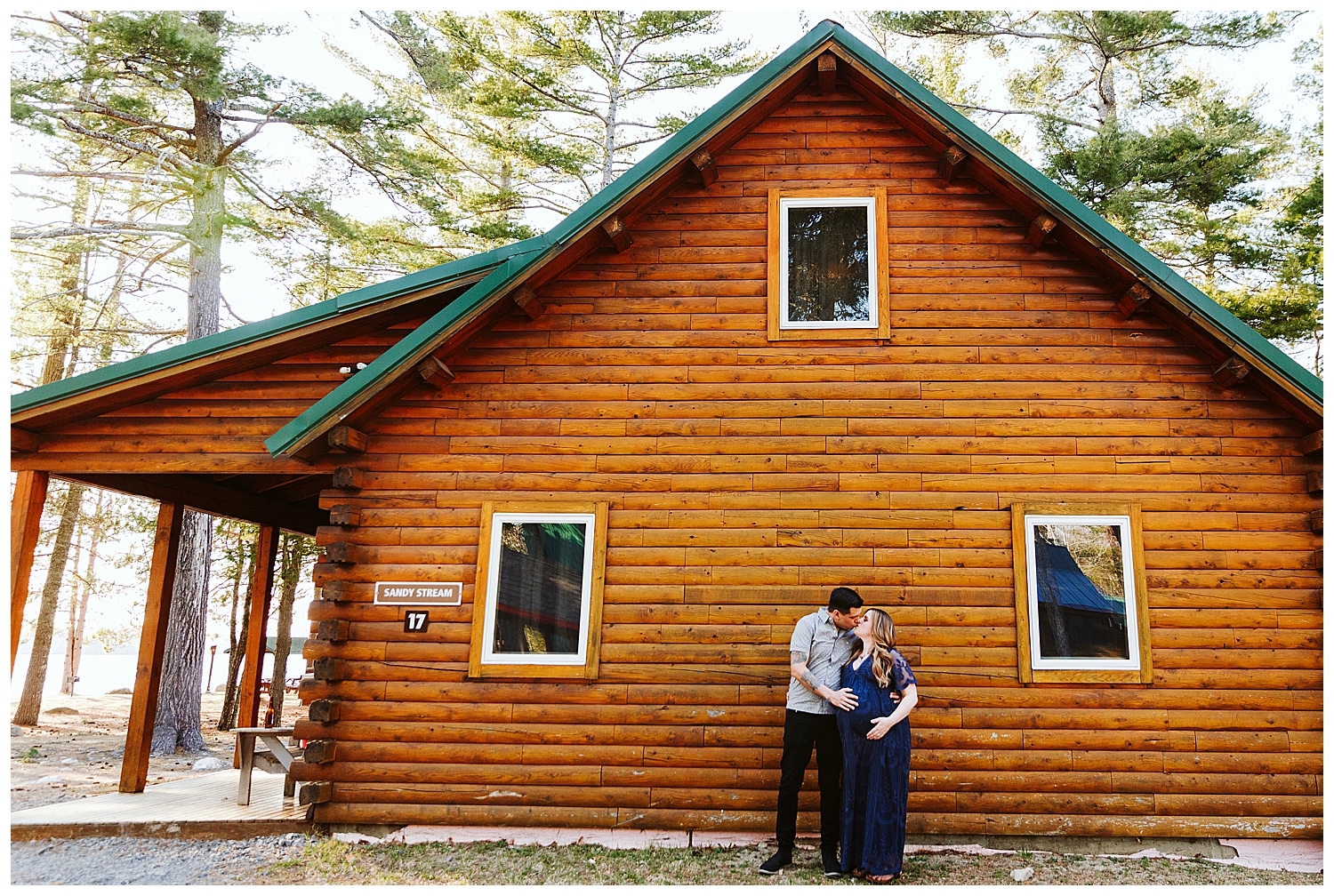 Expecting couple in front of log cabin in Millinocket Maine