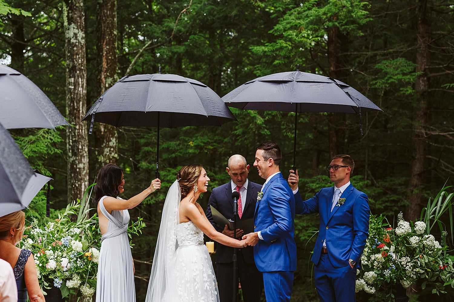 bridesmaid and groomsman hold umbrellas over bride and groom during wedding ceremony