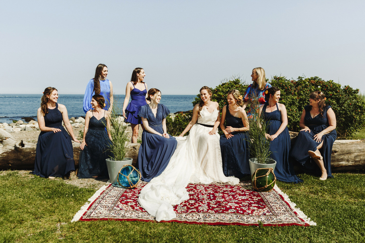 bride and bridesmaids sitting on driftwood at wedding at Seacoast Science Center in Rye, NH
