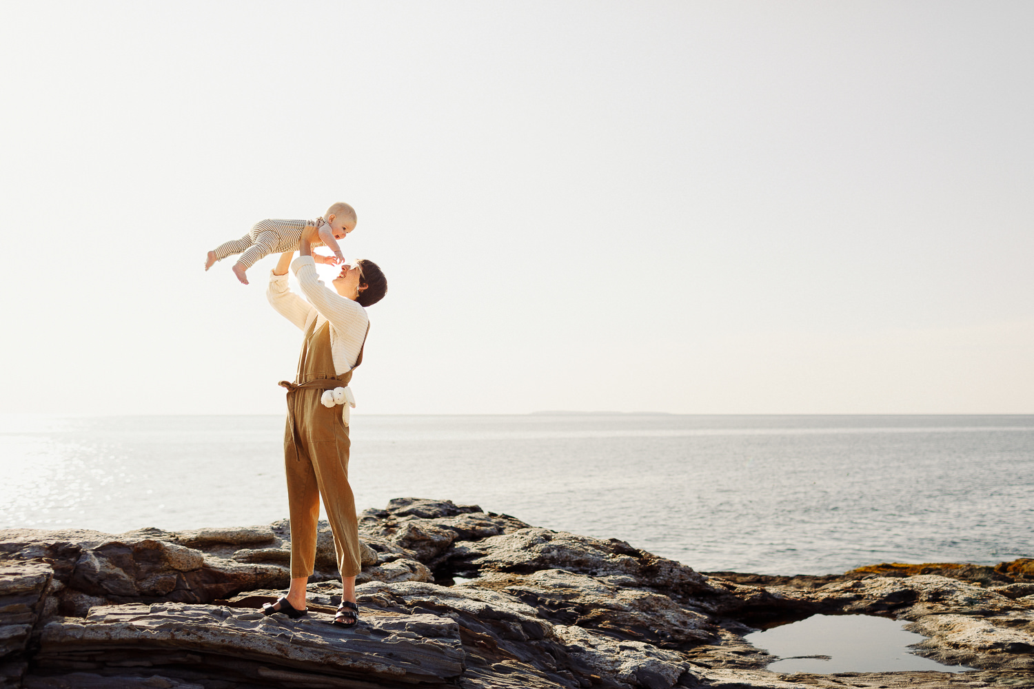 mother holding her baby in the air during summer portraits in Bristol, Maine