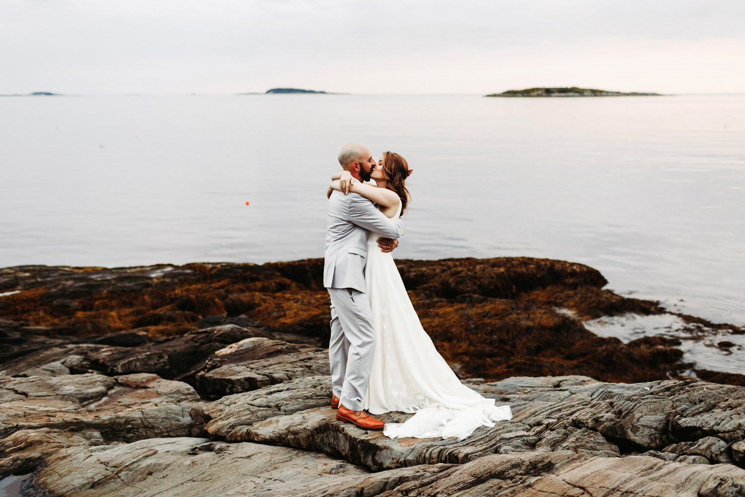 bride and groom kissing on cliffs at twilight during Orr's Island Maine Wedding