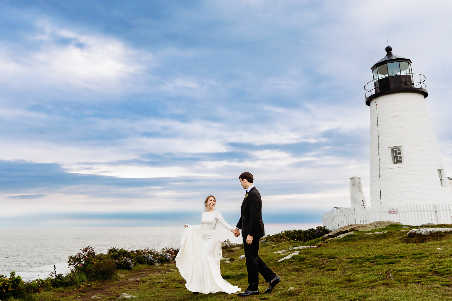 Bride and groom walking at Pemaquid Point Lighthouse during The Contented Sole Maine wedding