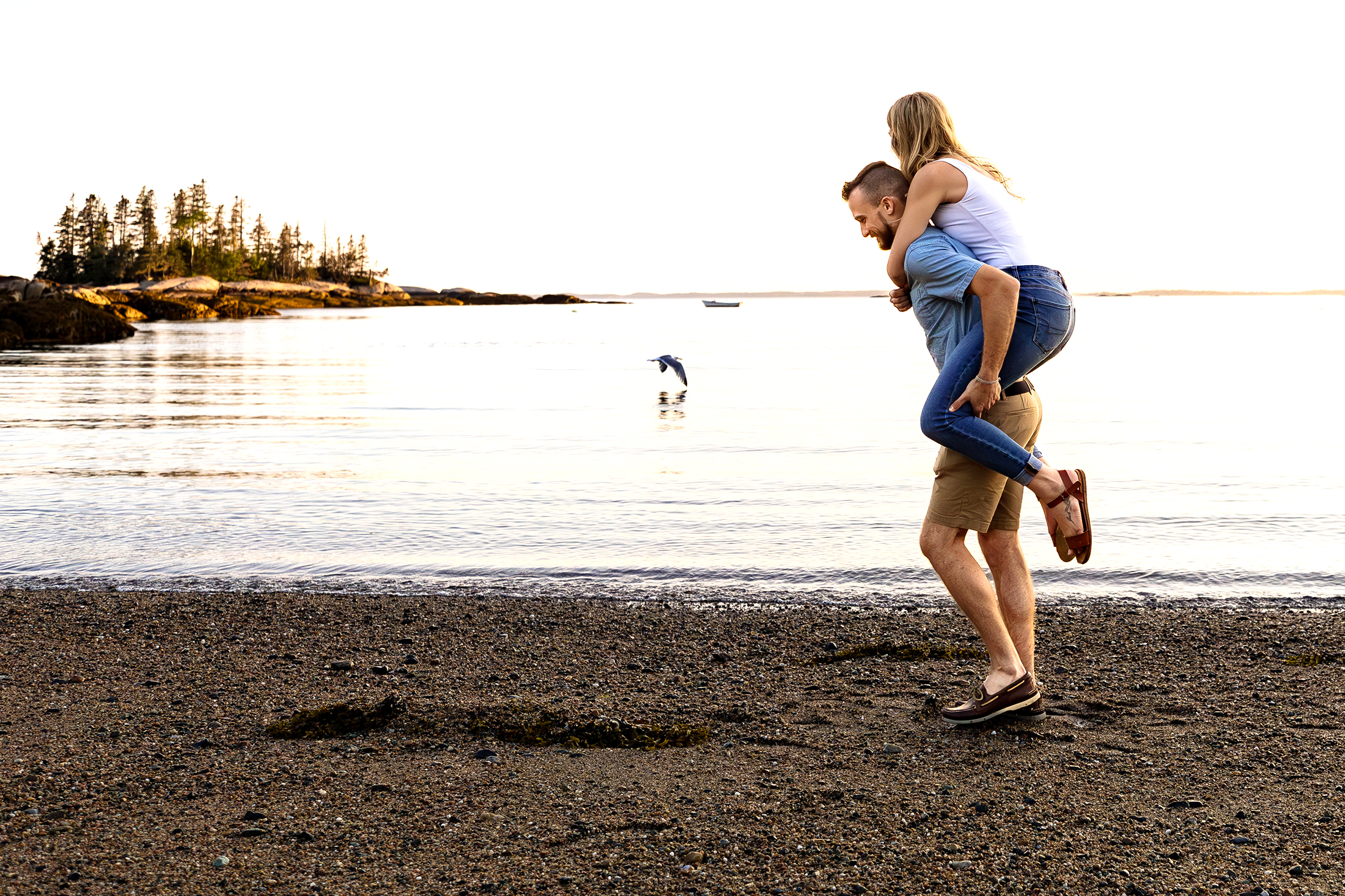 man giving fiancee a piggyback ride on Sand Beach in Stonington Maine