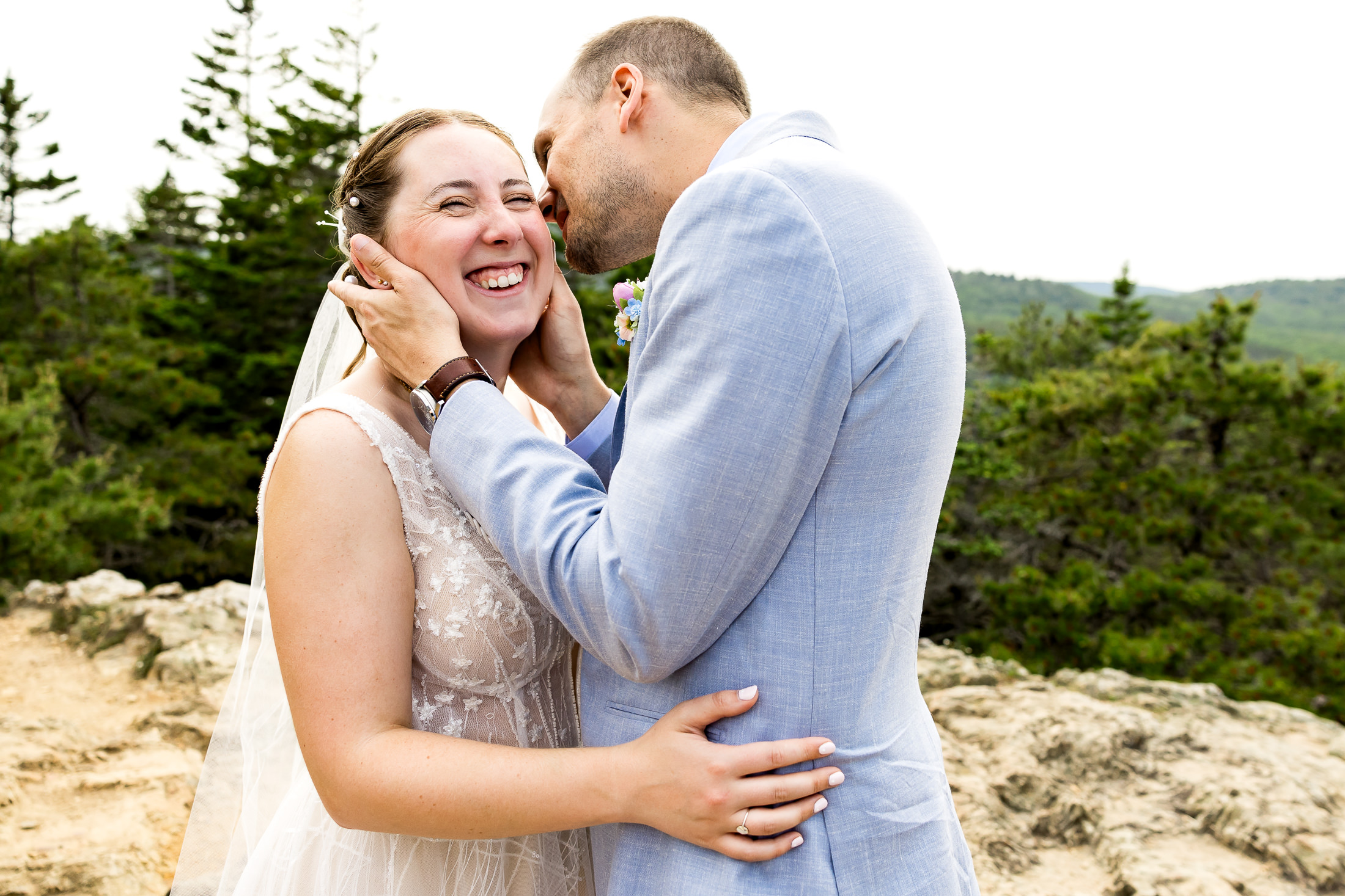 Bride laughing while groom whispers in her ears during Sand Beach Acadia wedding